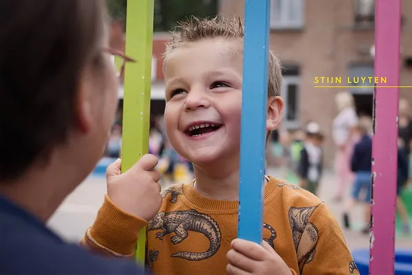 Kind aan schoolpoort die lacht naar mama